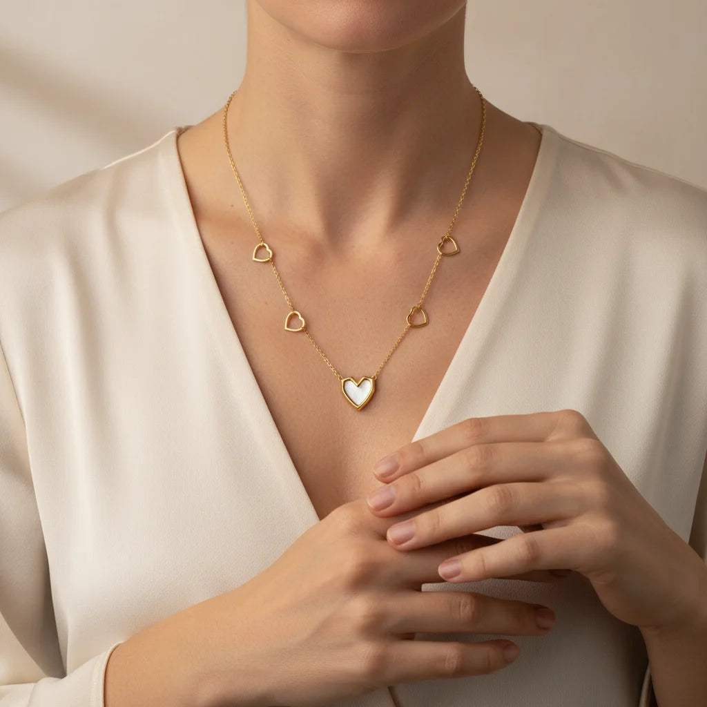 Gold necklace with heart pendants worn by a person in a white outfit.