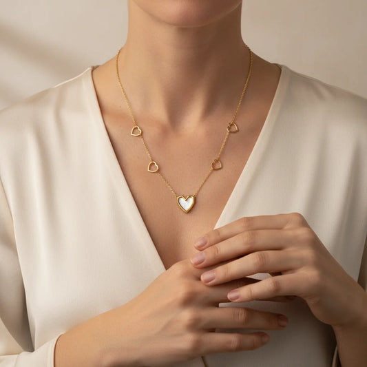 Gold necklace with heart pendants worn by a person in a white outfit.