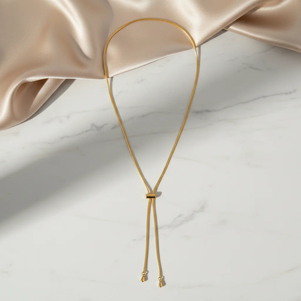 Gold necklace on a marble surface with a soft pink fabric background