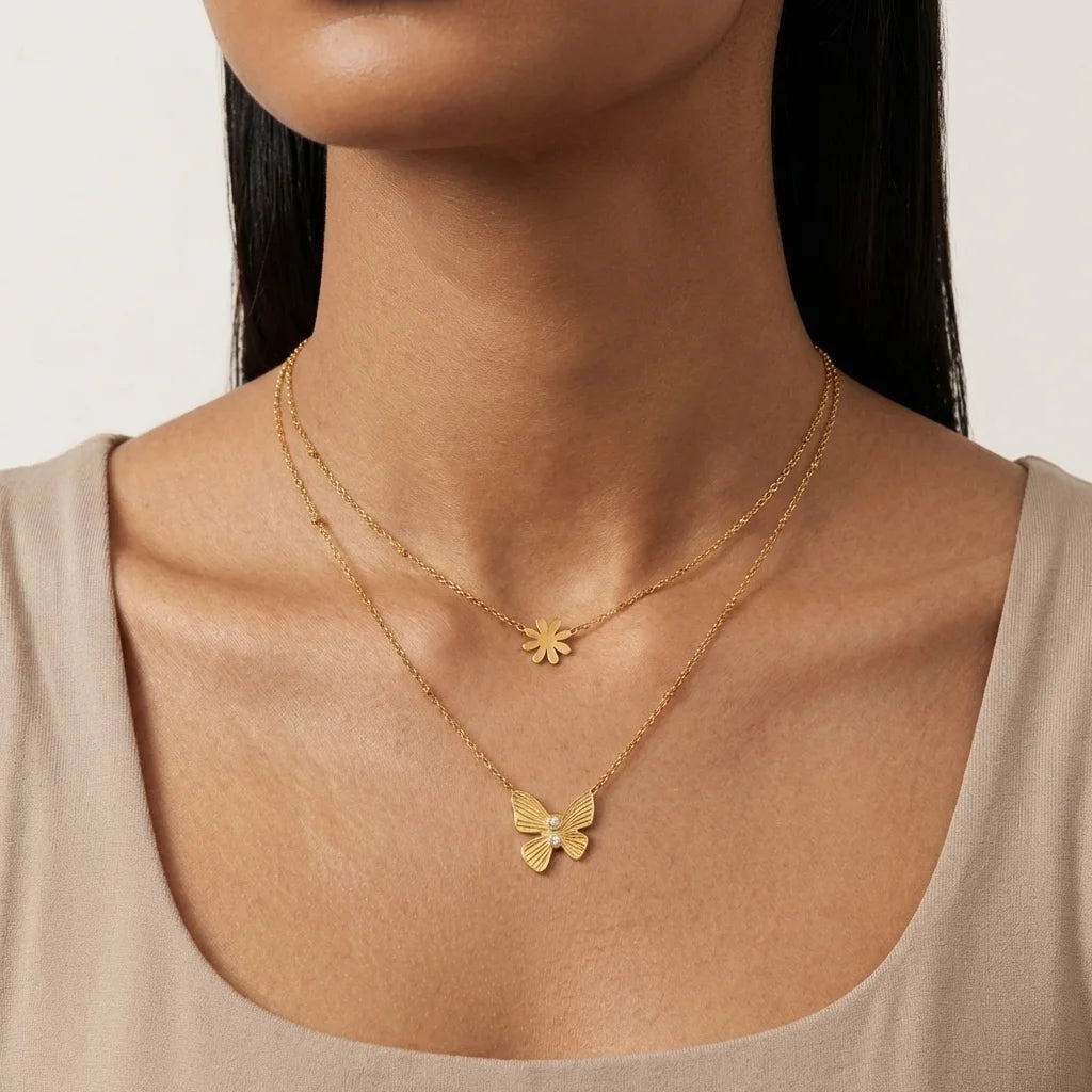 Gold necklaces with butterfly and flower pendants on a neutral background