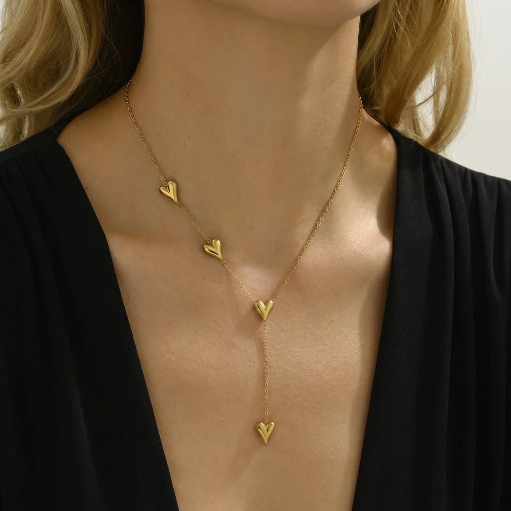 Gold necklace with heart-shaped pendants worn by a person against a neutral background