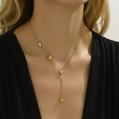 Gold necklace with heart-shaped pendants worn by a person against a neutral background