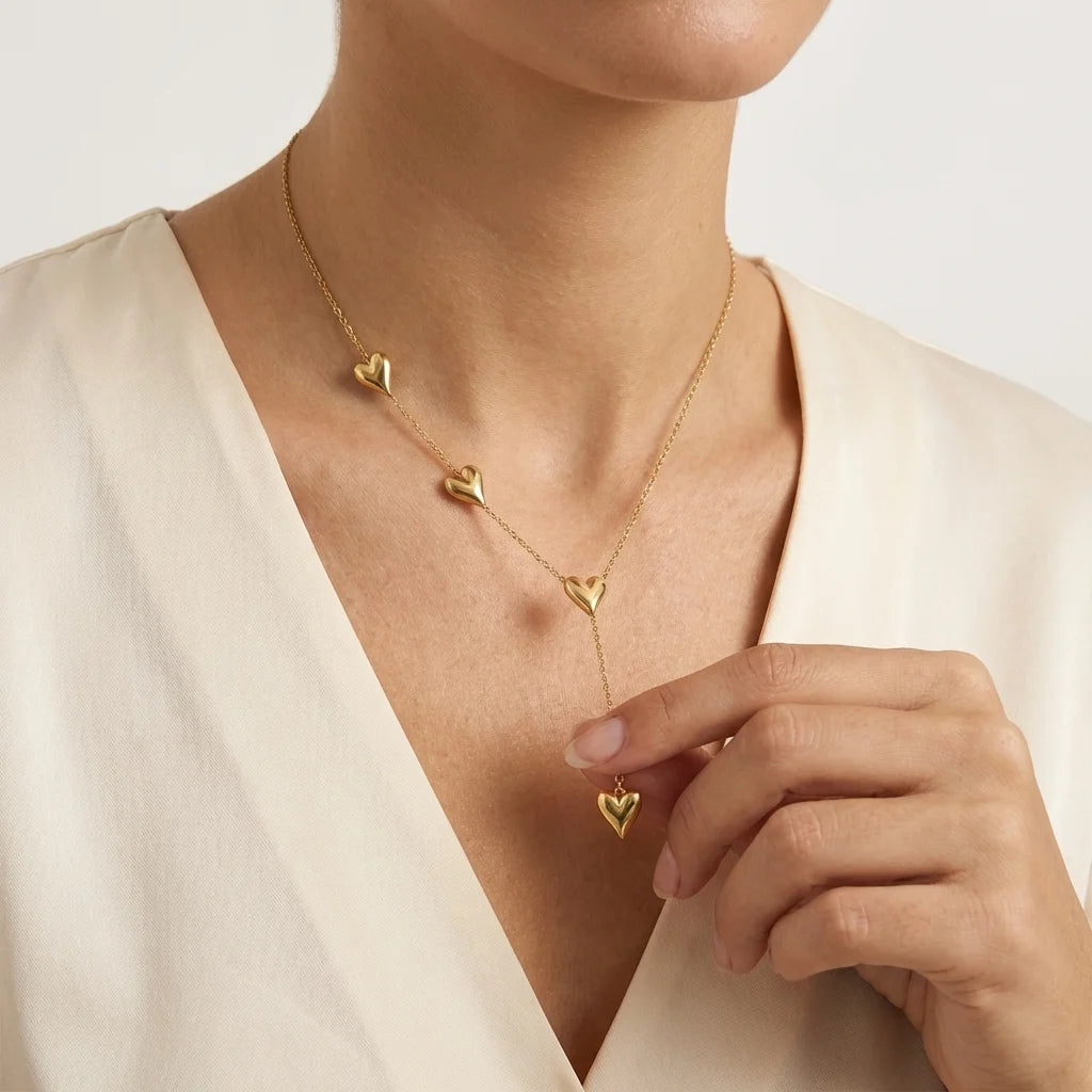 Gold heart-shaped necklace worn by a person against a neutral background