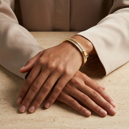 Close-up of hands wearing a gold bracelet on a beige surface