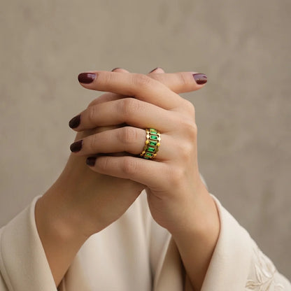 Hand wearing a green gemstone ring on a beige background