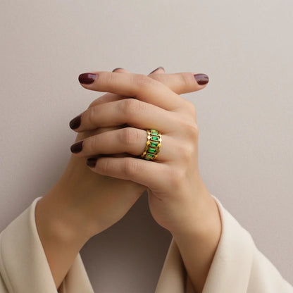 Hand wearing a green gemstone ring on a neutral background