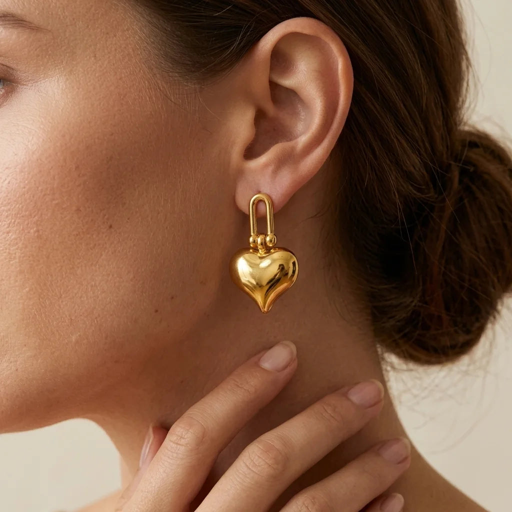 Gold heart-shaped earring worn by a person with a neutral background