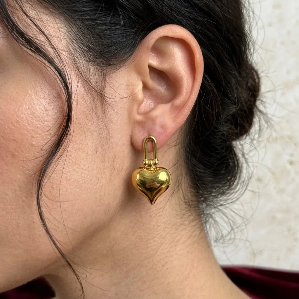 Gold heart-shaped earring worn by a person with a blurred background