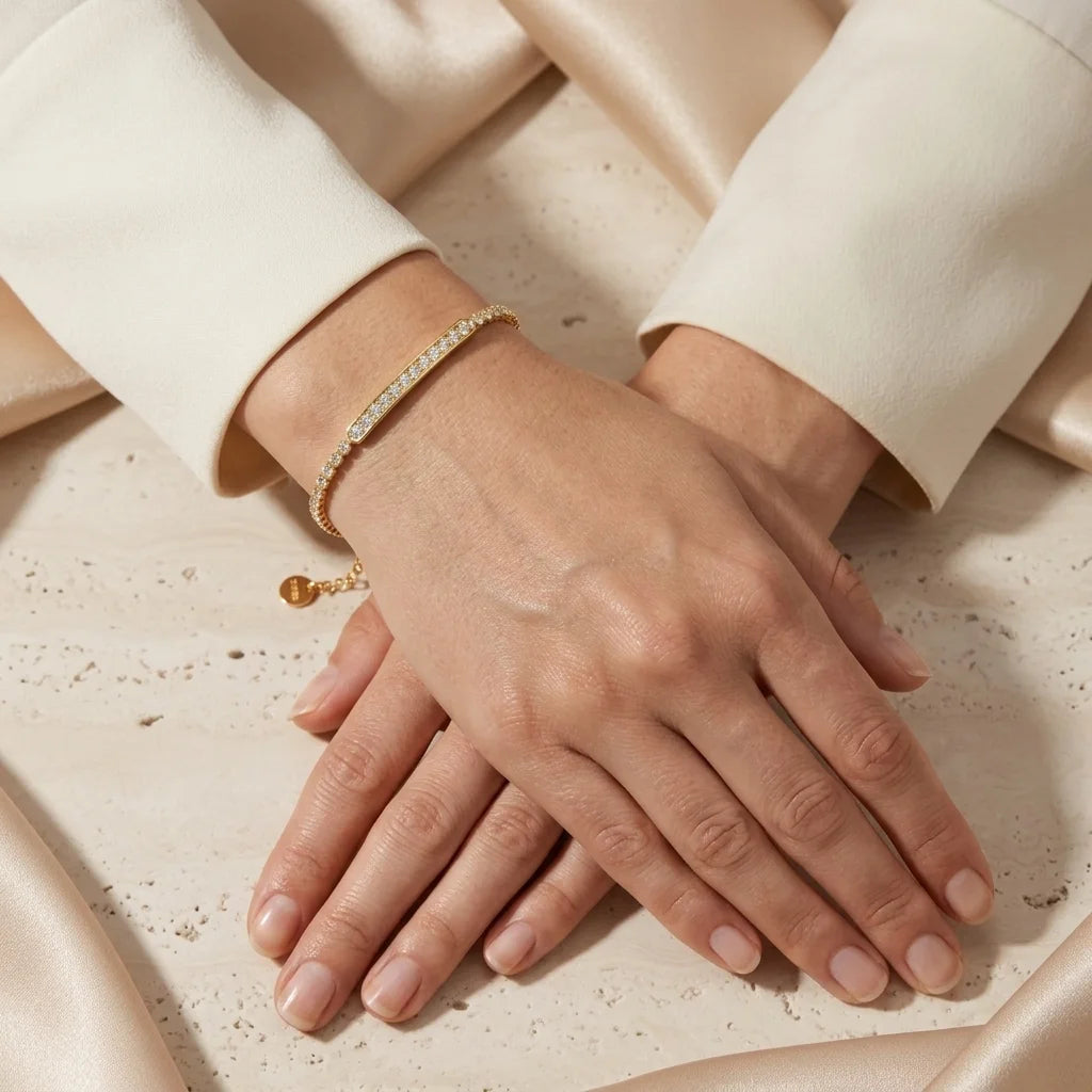 Close-up of hands wearing a gold bracelet on a neutral background
