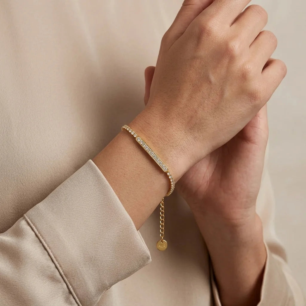 Gold bracelet with a pendant on a wrist against a beige background