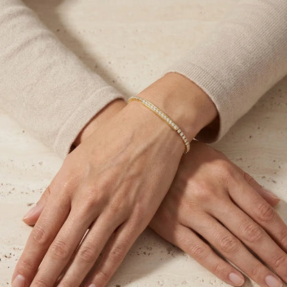 Close-up of hands wearing a gold bracelet on a neutral background