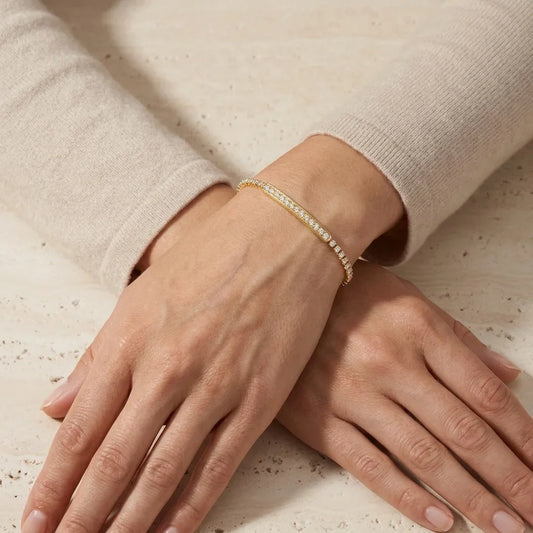 Close-up of hands wearing a gold bracelet on a neutral background
