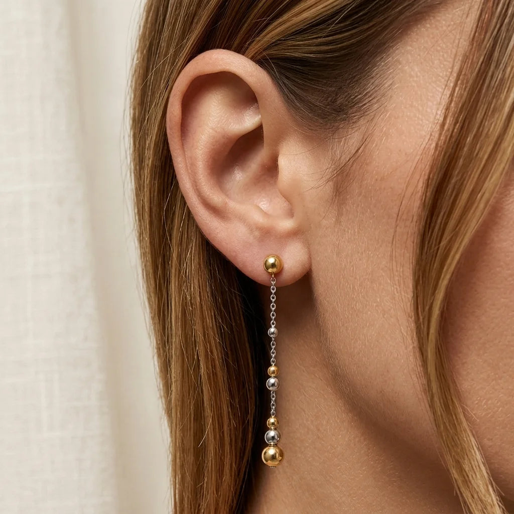 Close-up of an ear wearing a gold and silver bead earring against a neutral background