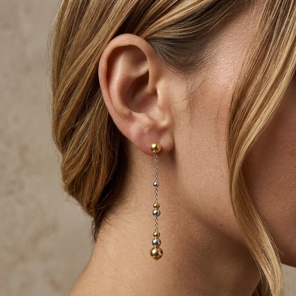 Close-up of an ear wearing a gold and silver bead earring against a neutral background