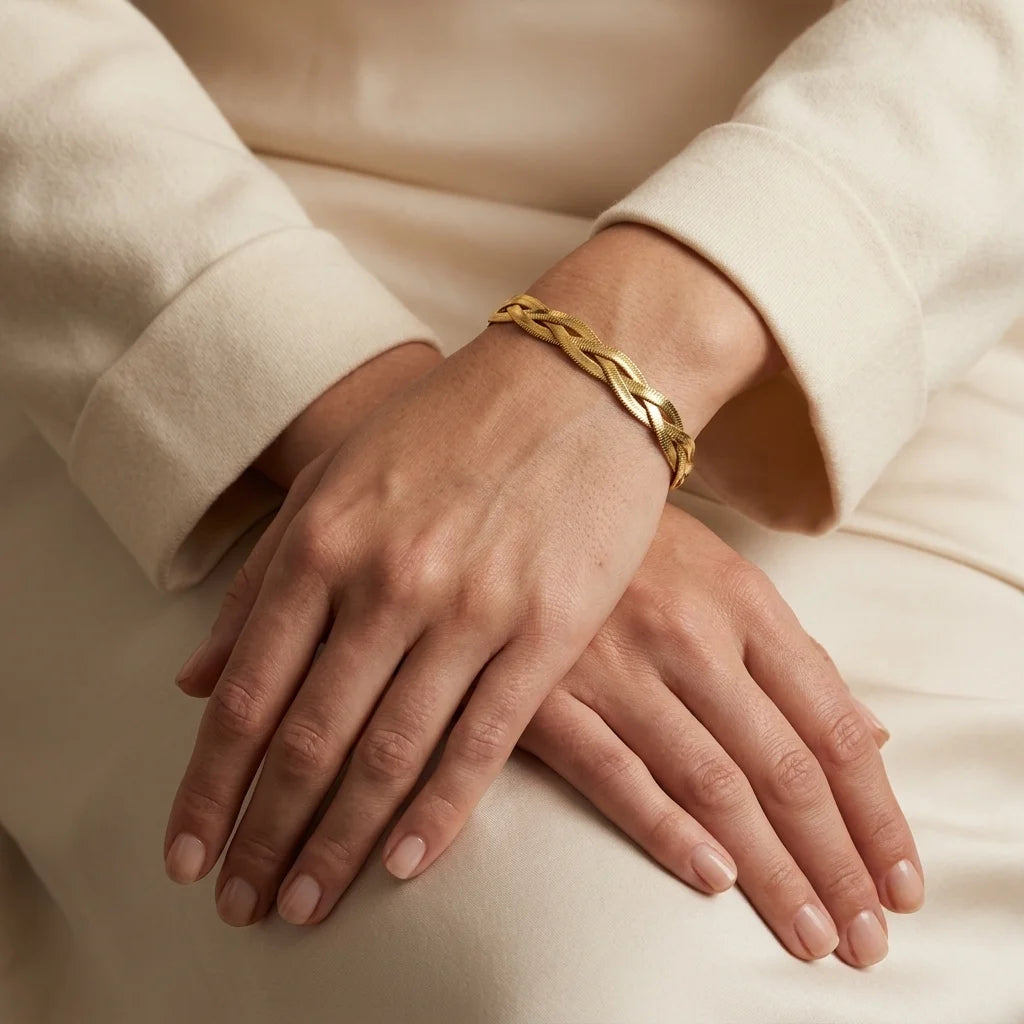 Close-up of hands wearing a gold bracelet on a neutral background