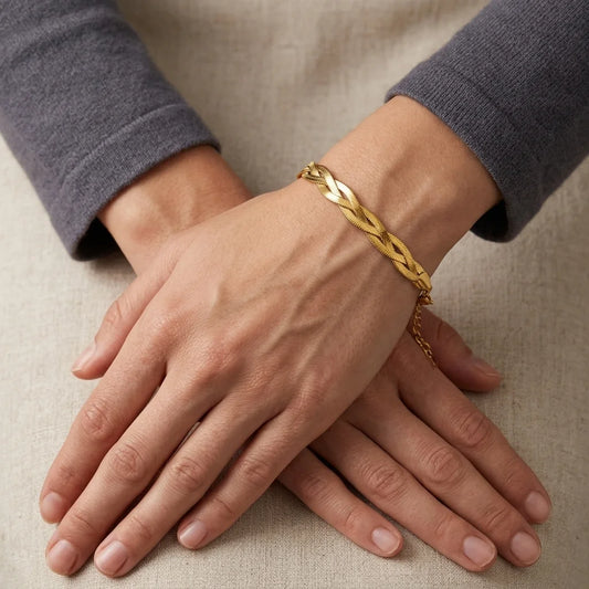 Gold bracelet on a person's wrist with hands resting on a beige surface