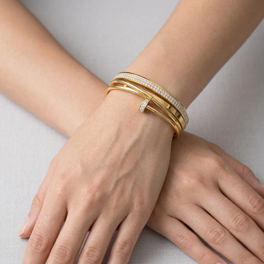 Gold bracelets on a person's wrist against a neutral background