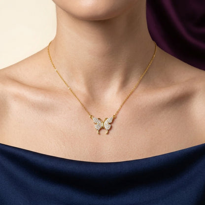 Gold butterfly necklace with diamonds on a person wearing a dark blue garment.