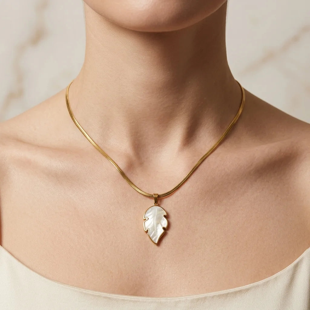 Gold necklace with a leaf-shaped pendant on a neutral background