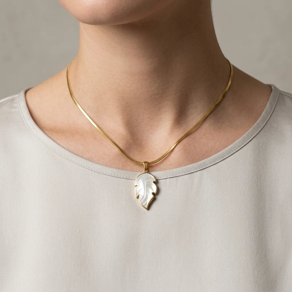 Gold necklace with a leaf-shaped pendant worn by a person on a neutral background