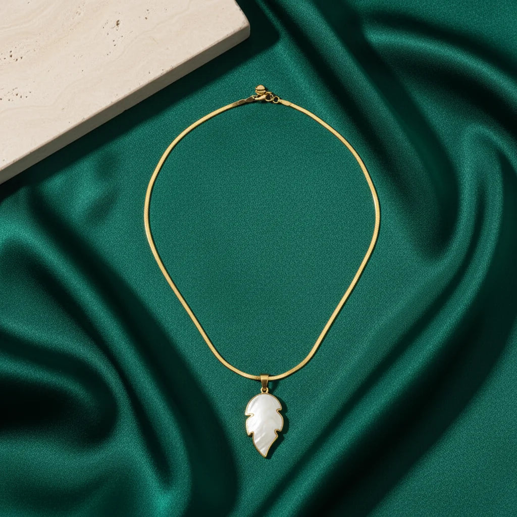 Gold necklace with a leaf-shaped pendant on a green fabric background