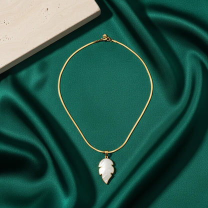Gold necklace with a leaf-shaped pendant on a green fabric background