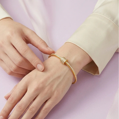 Gold bracelet on a hand against a light pink background