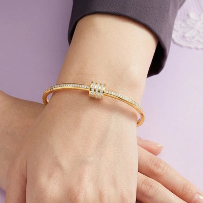 Gold bracelet on a hand against a light purple background