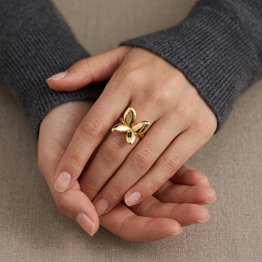 Gold butterfly ring on a person's finger against a neutral background