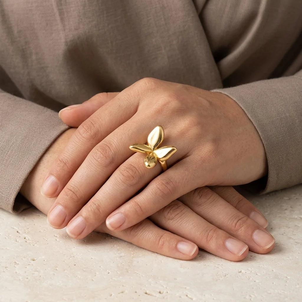 Gold butterfly ring on a hand with a neutral background