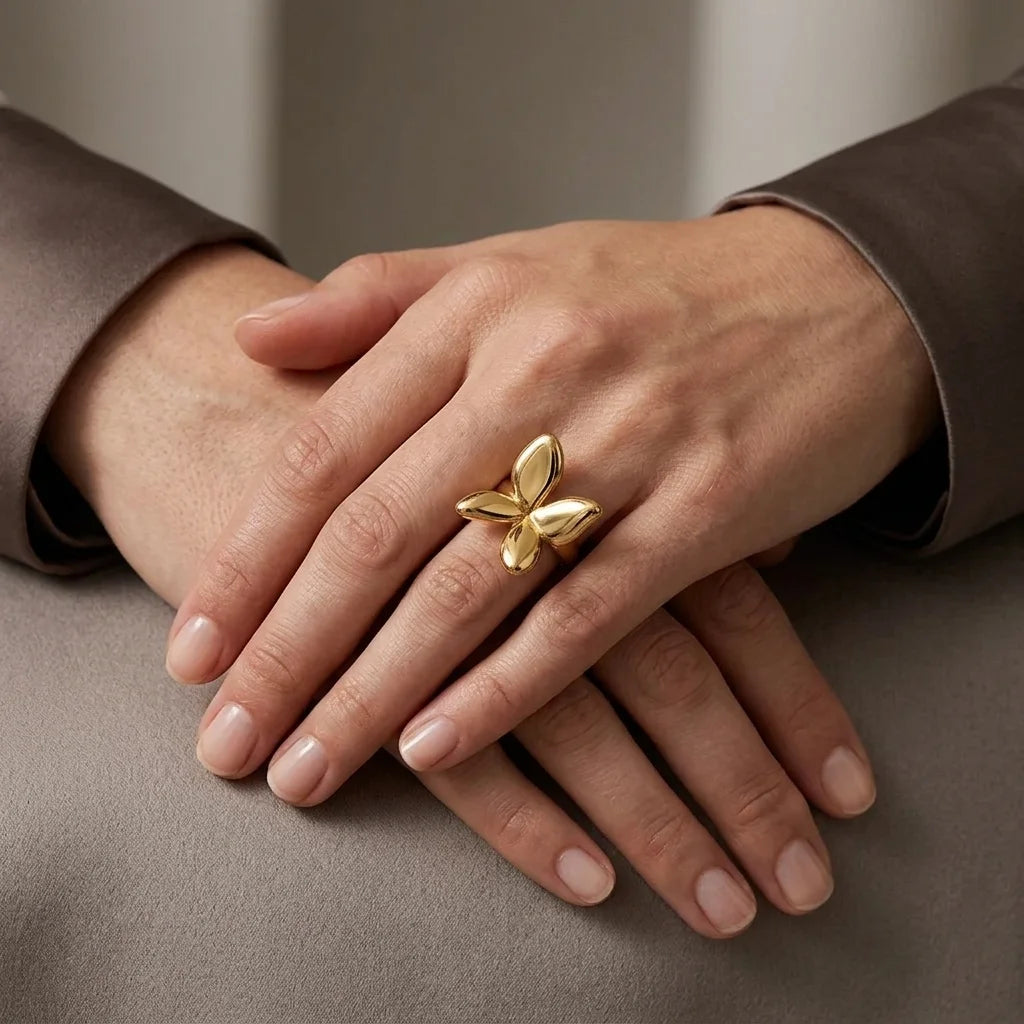 Gold butterfly ring on a person's finger with a neutral background