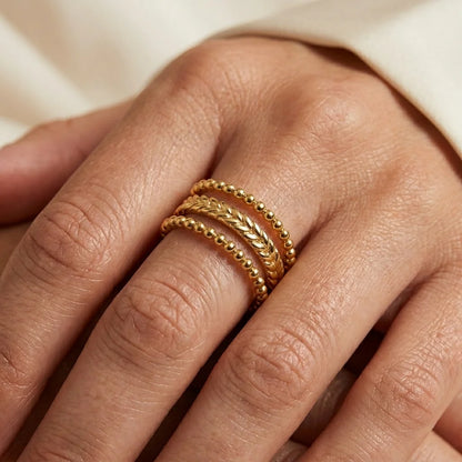 Close-up of a hand wearing two gold rings on a neutral background