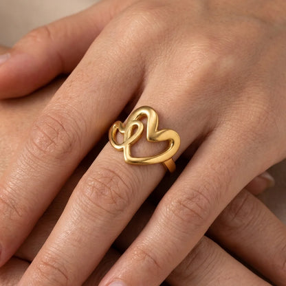 Gold heart-shaped ring on a person's finger against a neutral background