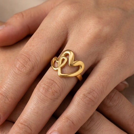 Gold heart-shaped ring on a person's finger against a neutral background