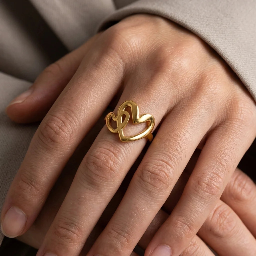 Gold heart-shaped ring on a person's finger against a neutral background