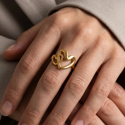 Gold heart-shaped ring on a person's finger against a neutral background