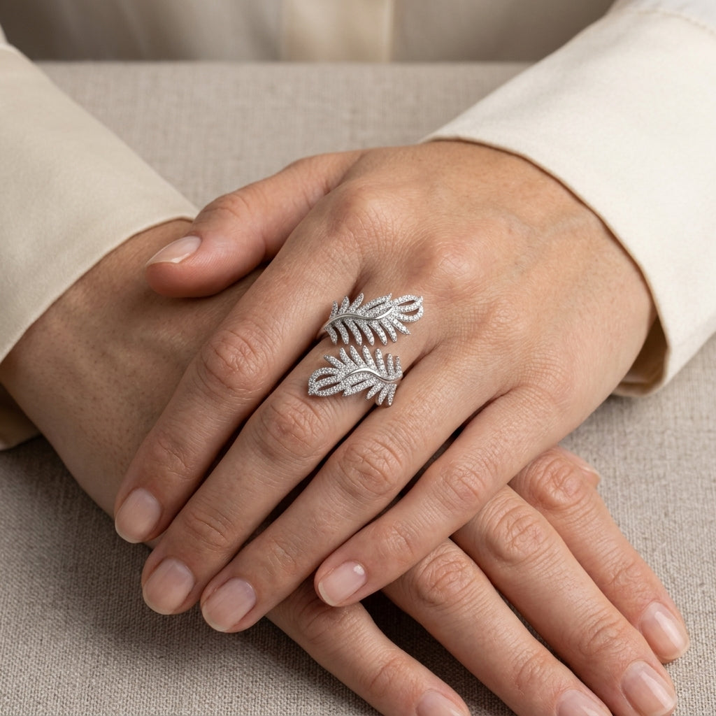 Silver feather-shaped ring on a person's finger with a neutral background