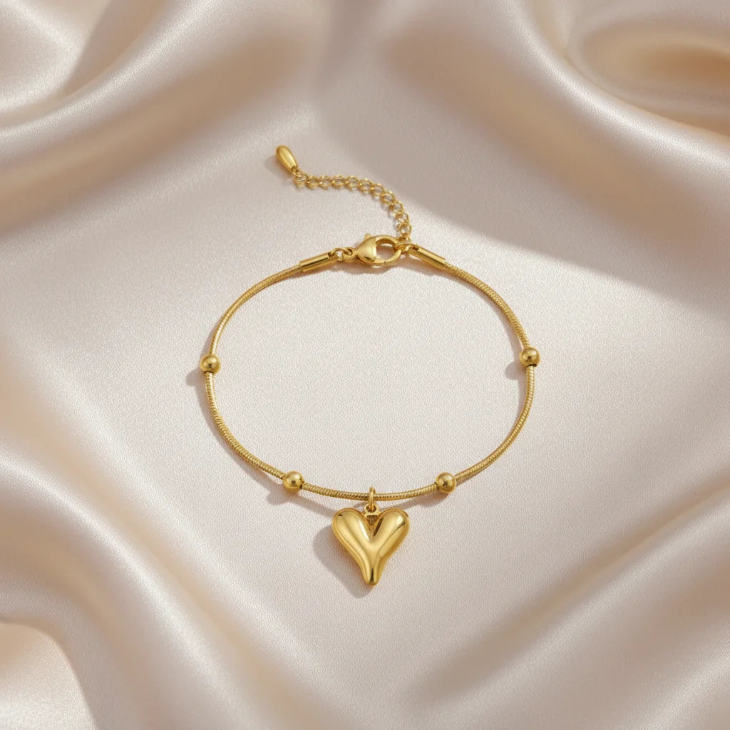 Gold bracelet with a heart charm on a satin surface