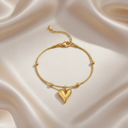 Gold bracelet with a heart charm on a satin surface