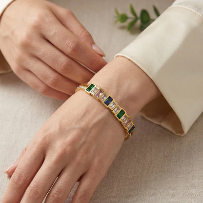 Gold bracelet with colorful gemstones on a person's wrist against a neutral background