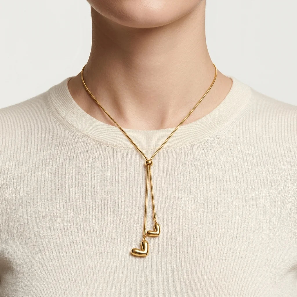 Gold necklace with heart pendants worn by a person on a plain background