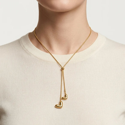 Gold necklace with heart pendants worn by a person on a plain background