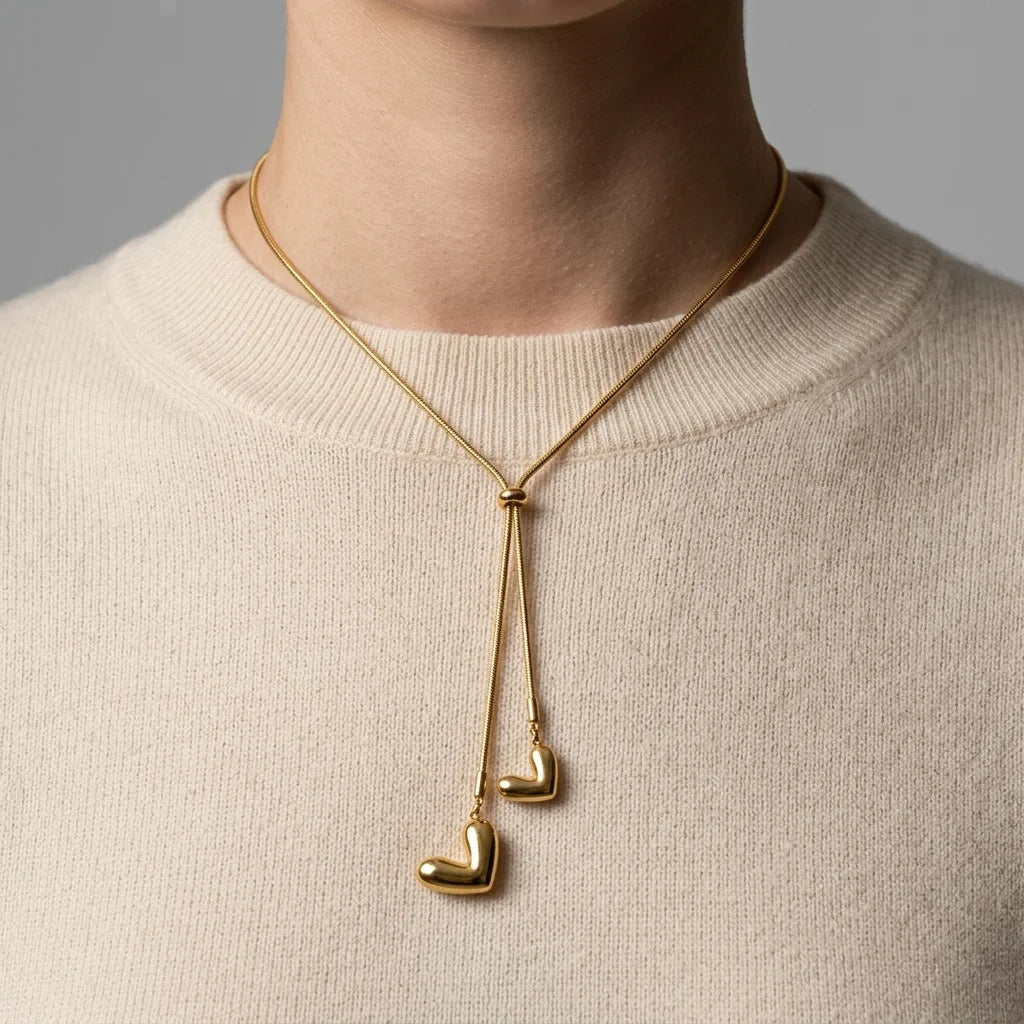 Gold necklace with heart pendants worn by a person in a beige sweater.