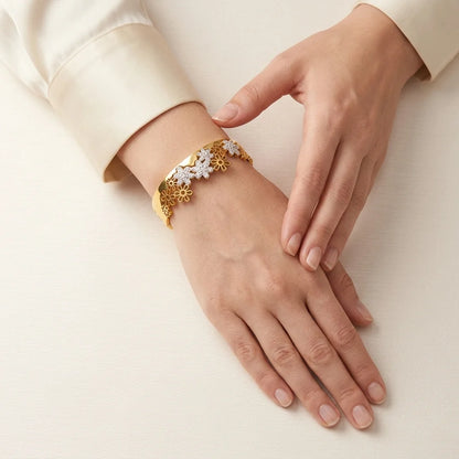 Gold bracelet with floral design on a hand against a beige background