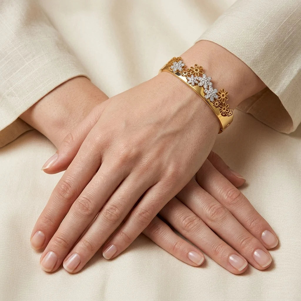 Close-up of a hand wearing a gold bracelet with floral design on a beige background