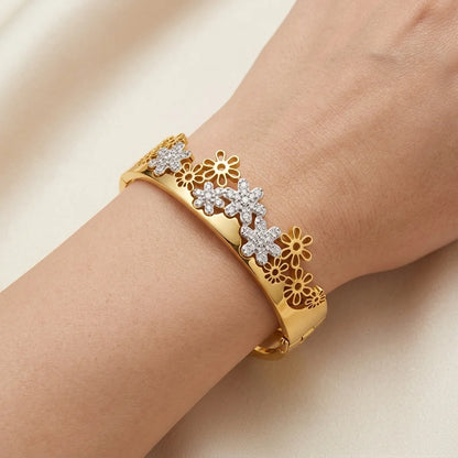 Gold bracelet with floral designs on a wrist against a beige background