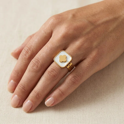 Hand wearing a gold ring with a square stone on a beige background