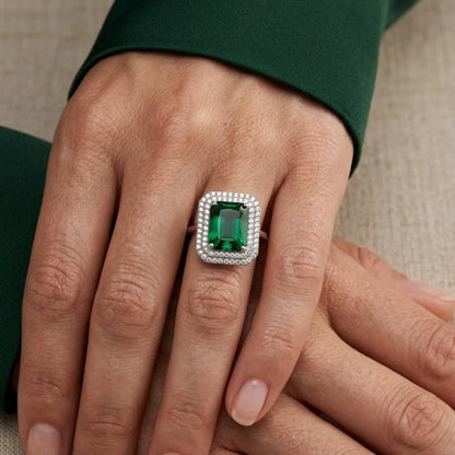 Close-up of a hand wearing a ring with a green gemstone on a neutral background