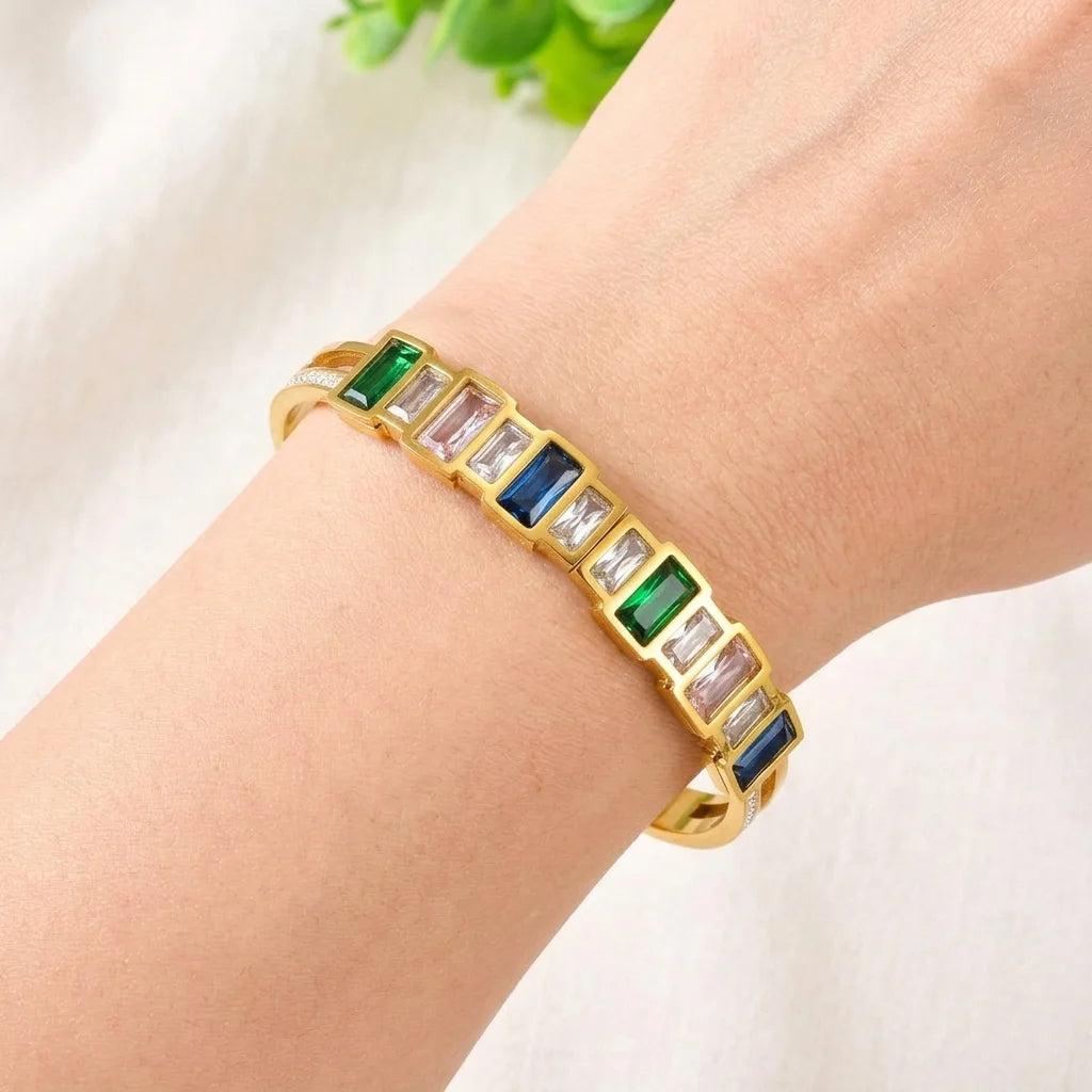 Gold bracelet with colorful gemstones on a wrist against a light background