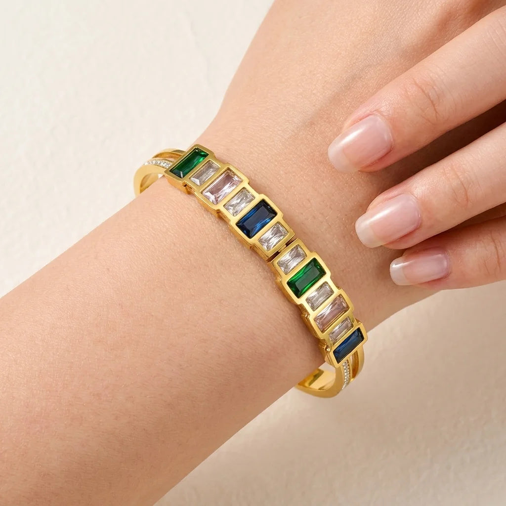 Gold bracelet with green and blue gemstones on a wrist against a beige background